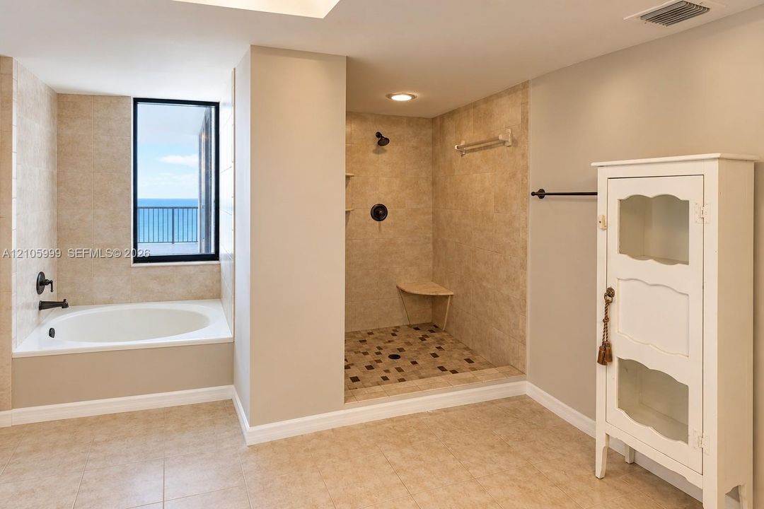 Bathroom featuring a drop-in soaking tub with a deck surround, a walk-in shower with a stone-tile floor and built-in bench, neutral wall-to-wall ceramic tile, and matte black fixtures