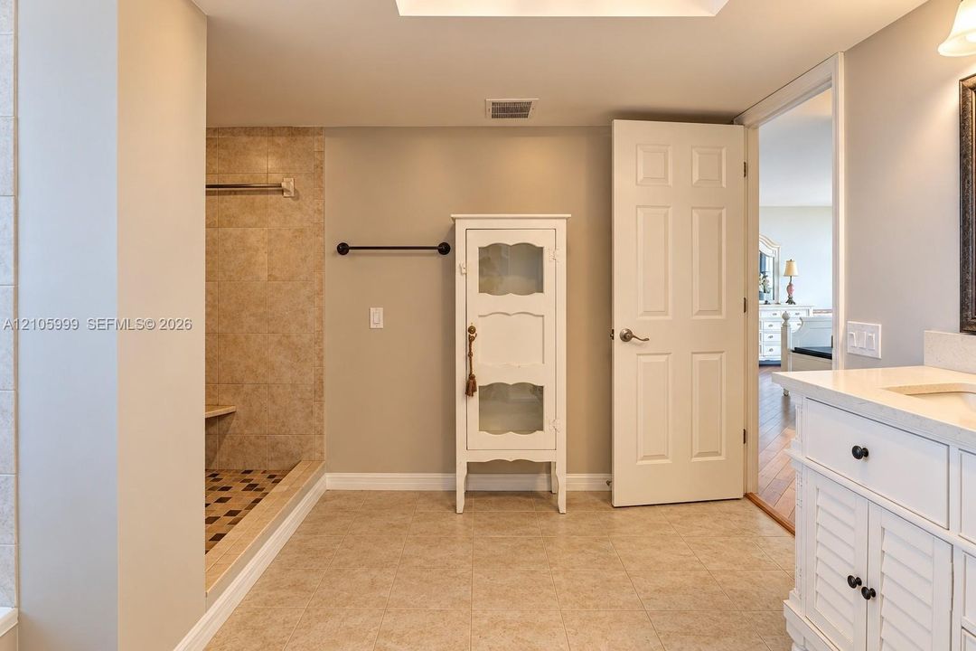 Bathroom featuring a walk-in shower with tiled surround, built-in vanity with countertop sink, and neutral tile flooring
