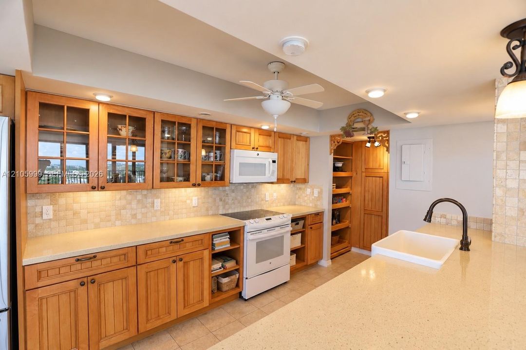 Kitchen featuring natural wood cabinetry, glass-front upper cabinets, stone-surfaced countertops, a farmhouse-style sink with a high-arch faucet, and an integrated pantry