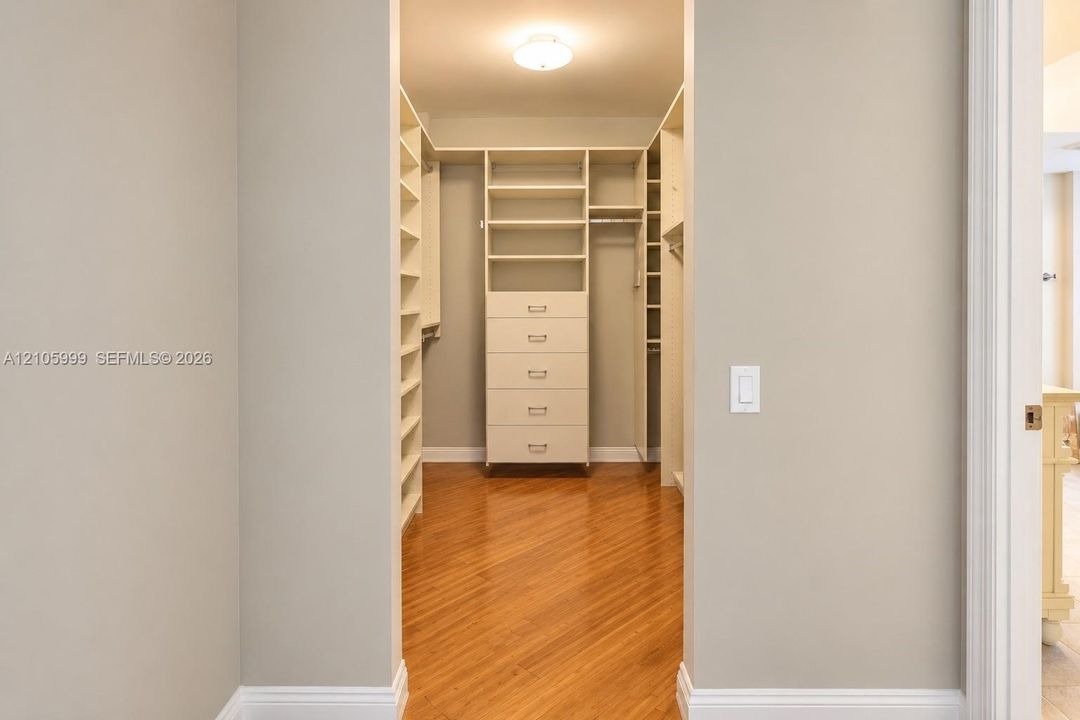 Walk-in closet featuring custom built-in cabinetry, five-drawer dresser unit, integrated shelving, and wood-finish flooring