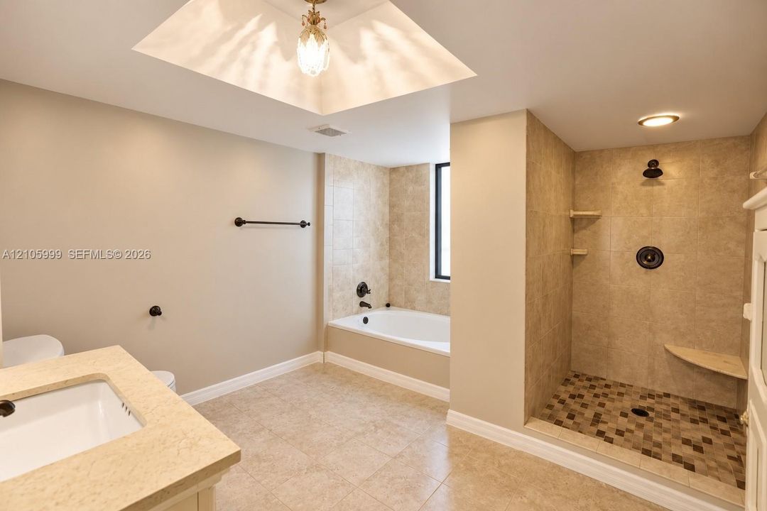 Bathroom featuring a walk-in shower with mosaic tile flooring, built-in bench seating, a soaking tub with tiled surround, and a vanity topped with a solid surface countertop