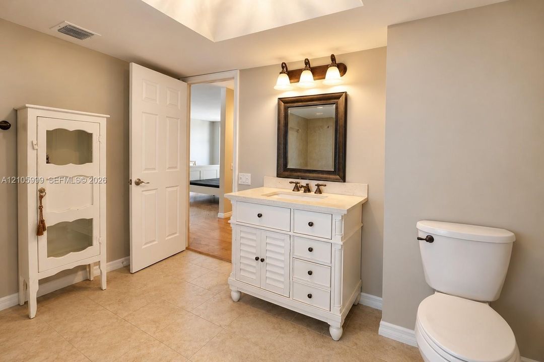 Bathroom featuring a white vanity with louvered-style cabinet doors, stone countertop with integrated sink, framed rectangular wall mirror, three-light vanity fixture, and tiled flooring