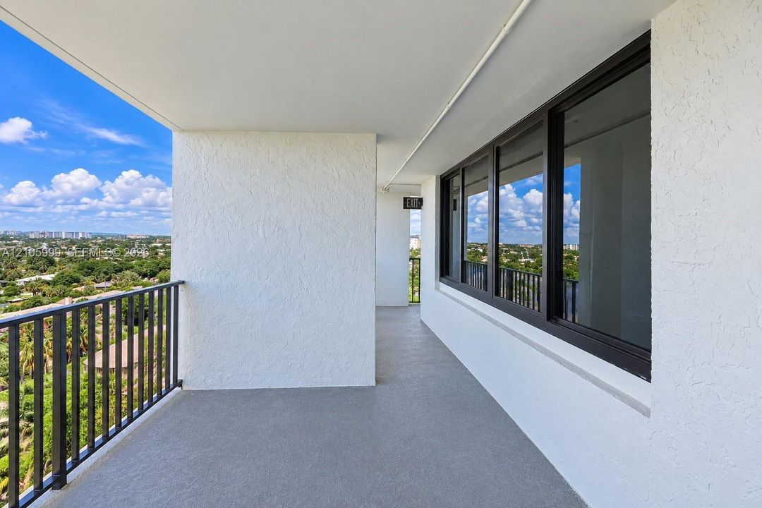 Covered balcony with textured stucco walls, dark-framed window panels, and black metal railings