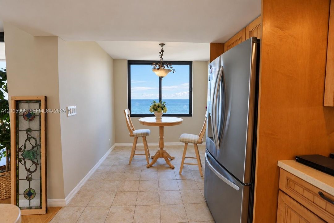 Kitchen nook area featuring natural-finish wood cabinetry, stainless steel refrigerator, tile flooring, and a large window with ocean scenery