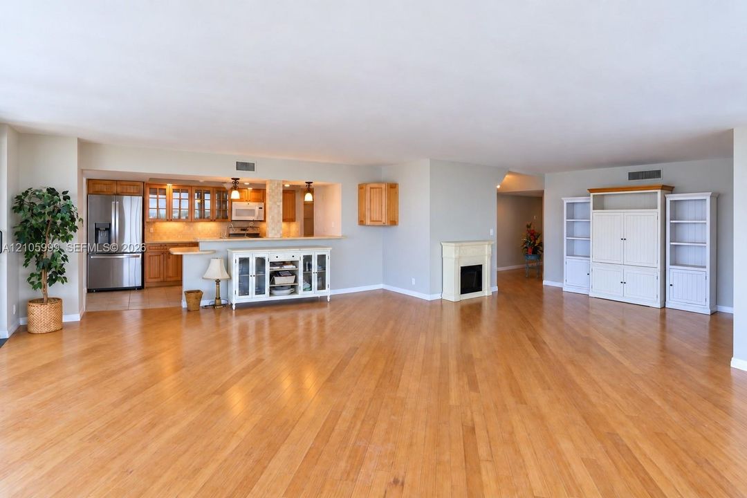 Open-concept area featuring wood-finish flooring, a kitchen with stainless steel appliances, a breakfast bar, and a fireplace with a mantel
