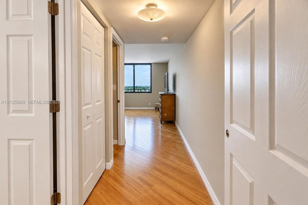 Interior hallway featuring wood-finish flooring, white six-panel doors, and a ceiling-mounted light fixture