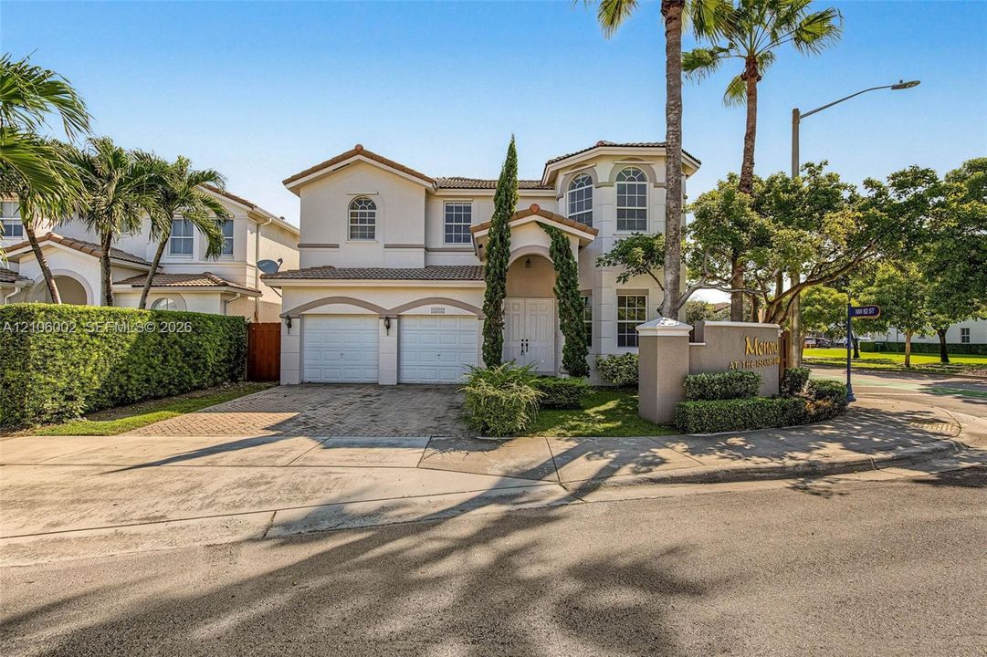 Two-story stucco exterior featuring arched windows, a multi-car garage, a paver driveway, and professional landscaping