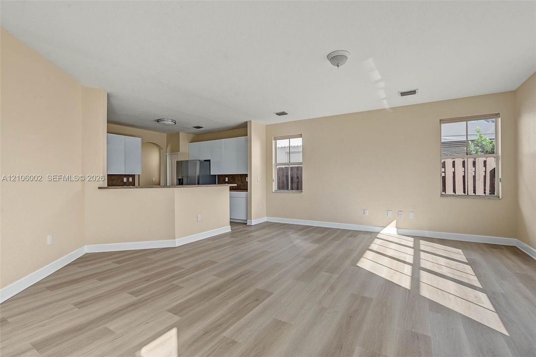 Open-concept space featuring wood-finish flooring, white cabinetry, a kitchen breakfast bar, and multiple windows