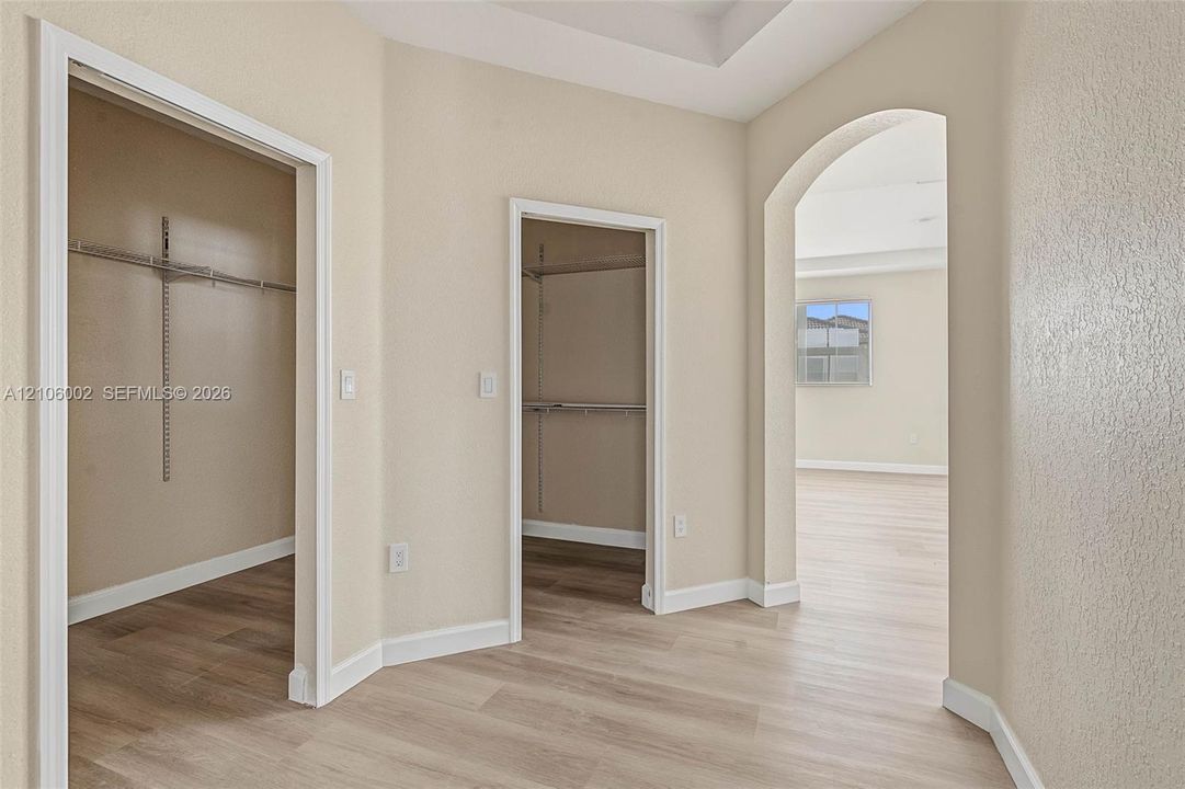 Neutral-toned interior featuring wood-finish flooring, two walk-in closets with built-in shelving, a tray ceiling, and an arched entryway