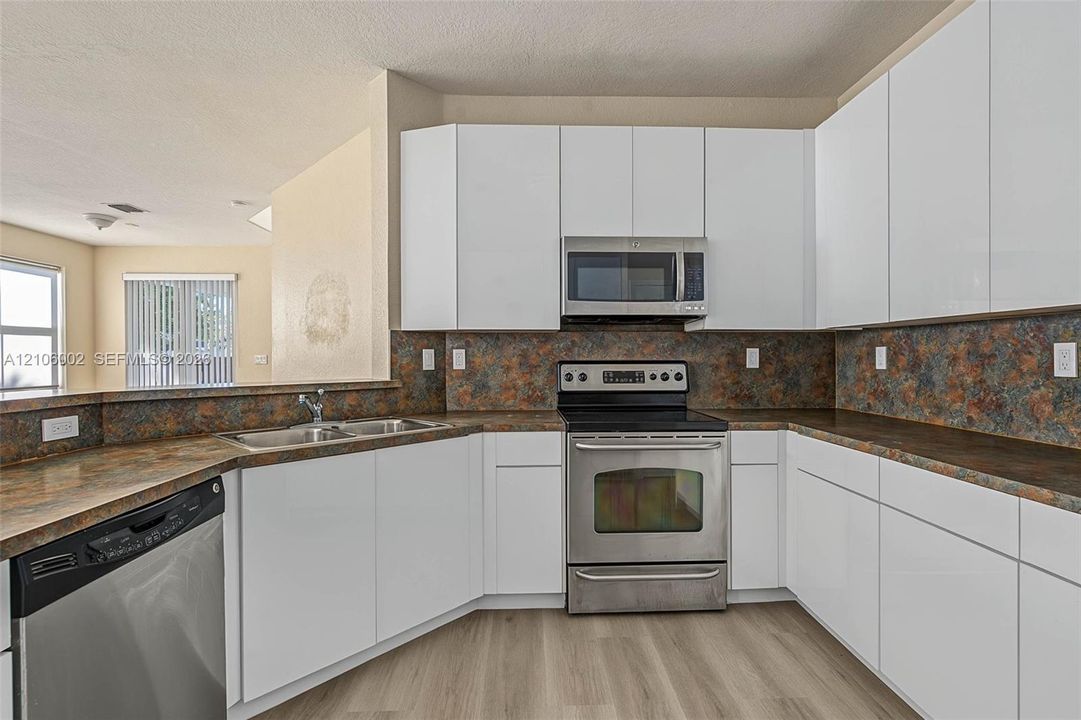 Kitchen featuring white flat-panel cabinetry, stainless steel appliances, speckled stone-finish countertops, full-height decorative backsplash, and wood-finish flooring