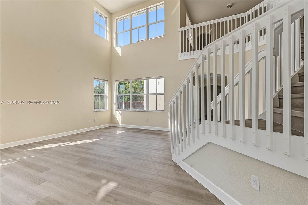 High-ceiling interior featuring multi-level windows, wood-finish flooring, and a white staircase with a balustrade railing
