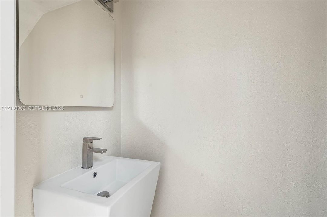 Wall-mounted rectangular basin with a single-handle metallic faucet, complemented by a square-cornered mirror and integrated lighting