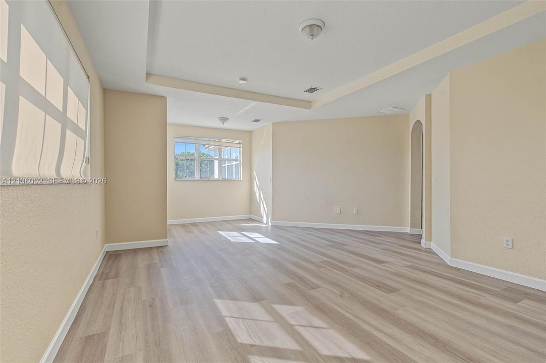 Spacious interior featuring wood-finish flooring, recessed tray ceiling, neutral wall tones, multi-pane windows, and an arched entryway