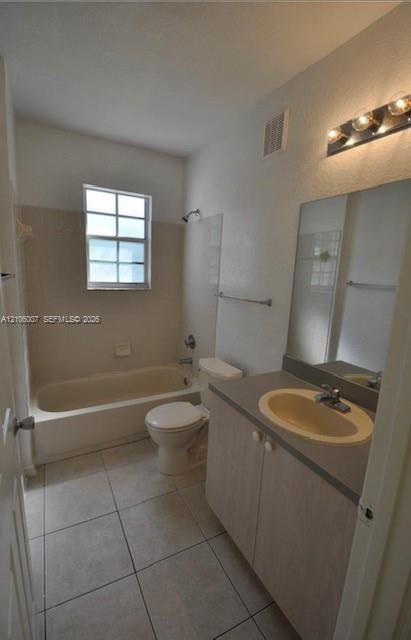 Bathroom featuring tile flooring, a tub-shower combination with tiled walls, a vanity with a solid-surface countertop, an integrated sink, and a wall-mounted light fixture