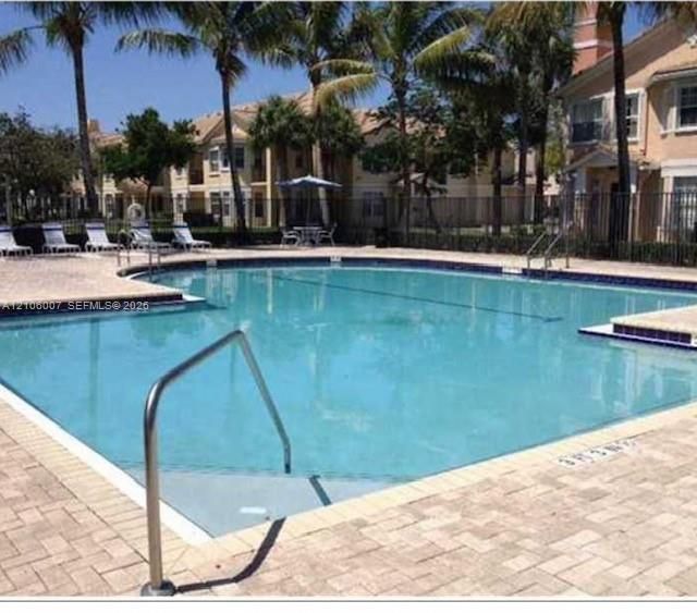 Outdoor swimming pool featuring paver stone decking, metal handrails, and mature palm trees