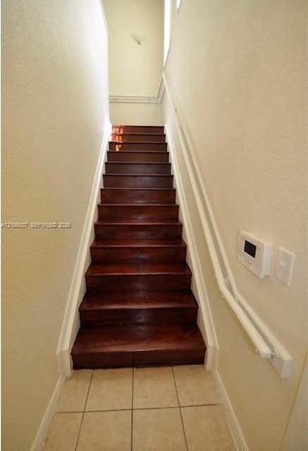 Staircase with dark-stained wood treads, neutral tile flooring, white-painted walls, and a white metal handrail