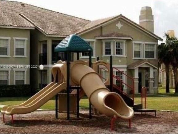 Multi-unit structure featuring a multi-gabled roofline, beige stucco facade, decorative chimney stack, and multi-paned windows, situated near a playground area