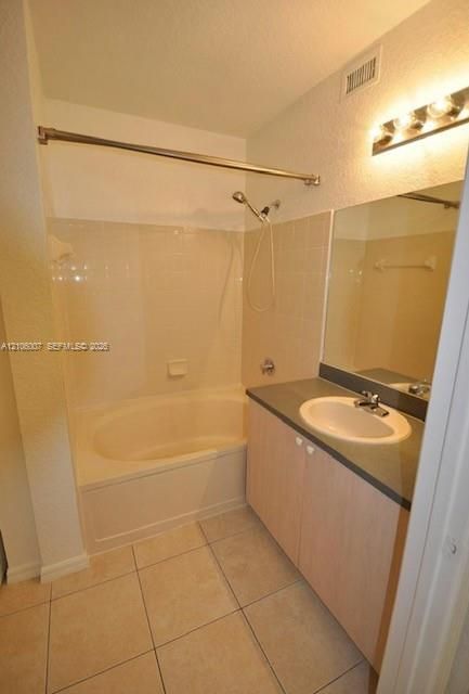 Bathroom featuring a vanity with a solid-surface countertop, an integrated oval sink, a wall-mounted vanity light, tile flooring, and a combined tub and shower enclosure with wall tiling
