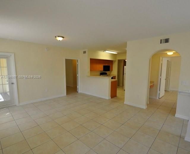 Open-concept interior featuring neutral tile flooring, arched wall detailing, wood-finish cabinetry, a pass-through breakfast bar, and a multi-pane glass door