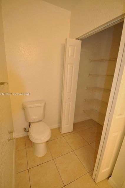 Ceramic tile flooring, white porcelain toilet, and walk-in storage area featuring built-in wire shelving and a bi-fold door