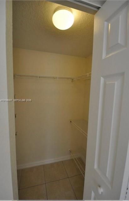 Storage space featuring tile flooring, white interior walls, wire shelving, and a ceiling-mounted light fixture