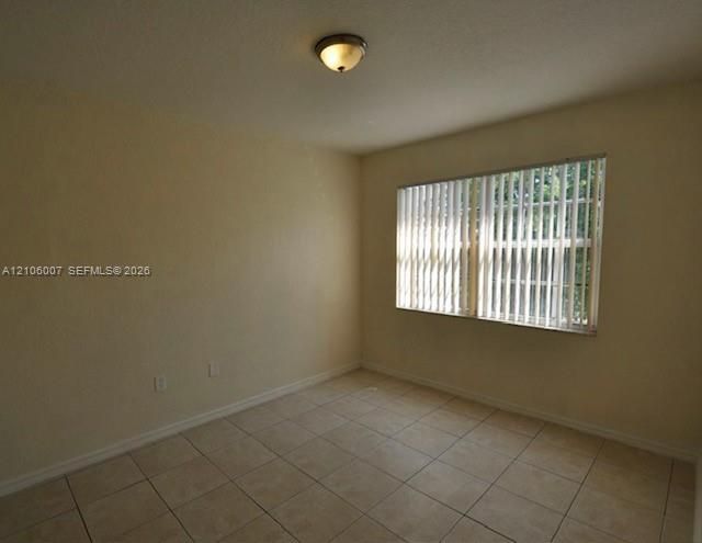 Neutral-toned interior space featuring light-colored ceramic tile flooring, a horizontal window with vertical blinds, and a circular flush-mount ceiling light fixture