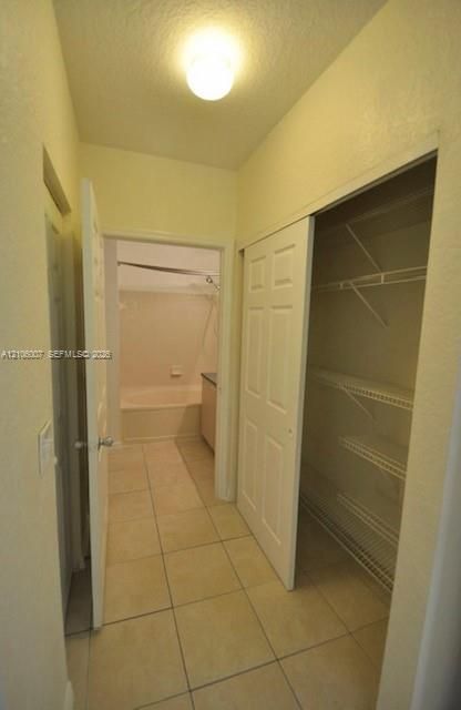 Neutral ceramic tile flooring, sliding panel closet doors with wire shelving, and overhead flush-mount lighting