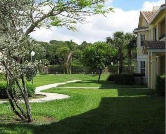 Expansive green space featuring a concrete pathway, mature trees, manicured lawn, and exterior siding with tiled roof elements