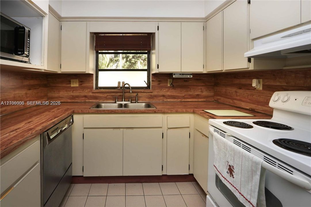 Kitchen featuring wood-finish countertops, tile flooring, flat-panel cabinetry, stainless steel dishwasher, and stainless steel double-basin sink with a gooseneck faucet