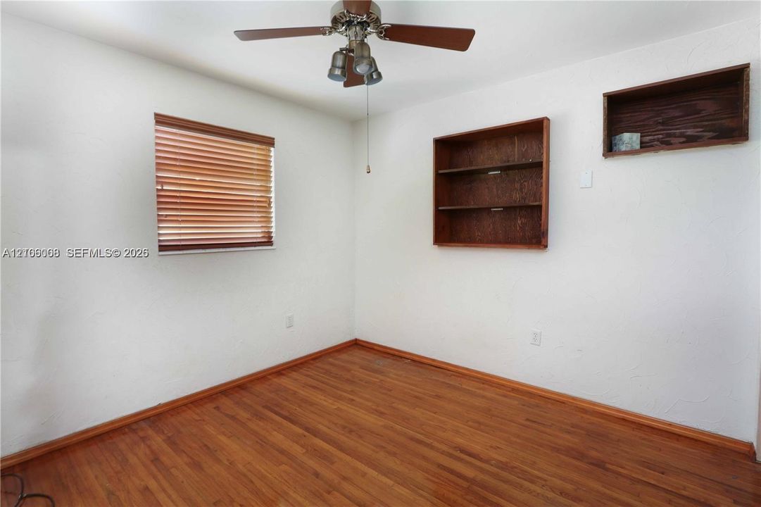 Room featuring wood-finish flooring, a ceiling fan with integrated lighting, window blinds, and built-in wall shelving