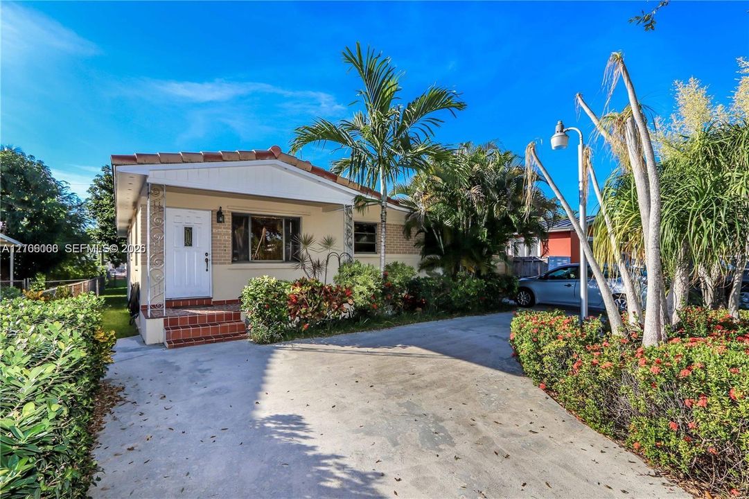 Single-story exterior featuring a concrete driveway, terracotta-toned masonry entrance steps, and manicured landscaping including established palm trees