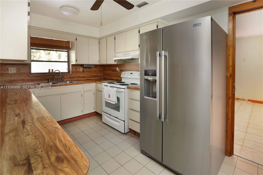 Kitchen featuring light-toned cabinetry, wood-finish countertops, tile flooring, and a stainless steel refrigerator
