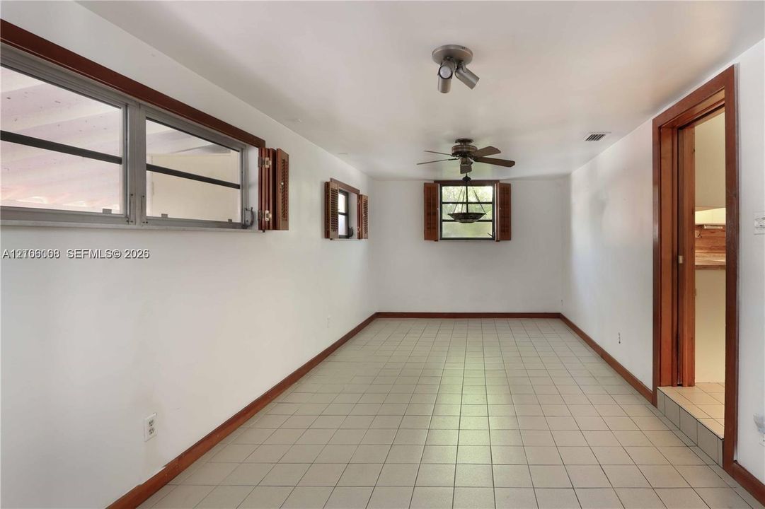 Interior space featuring neutral tile flooring, horizontal sliding windows, wood-finish window casings, a multi-blade ceiling fan, and track lighting