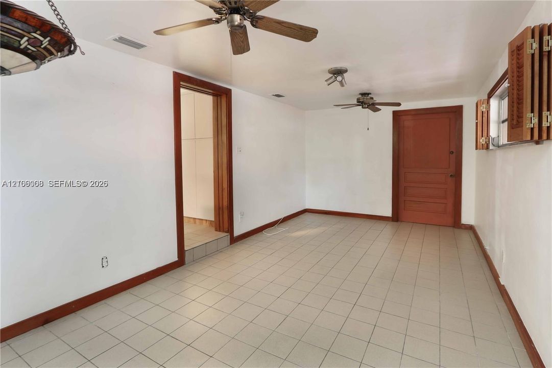 Interior space featuring ceramic tile flooring, two ceiling fans, wood-trim door casing, and wood-framed window shutters