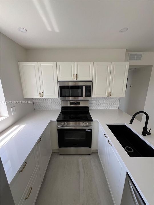 Kitchen featuring white cabinetry, quartz countertops, a hexagonal tile backsplash, stainless steel appliances, and a matte black faucet with an integrated undermount sink