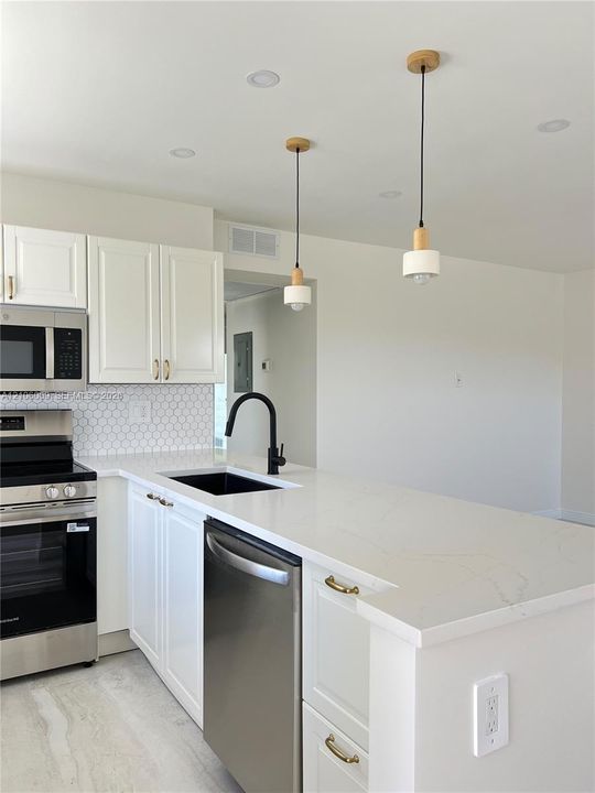 Kitchen featuring white cabinetry, quartz countertops, a hexagonal tile backsplash, stainless steel appliances, and matte black plumbing fixtures