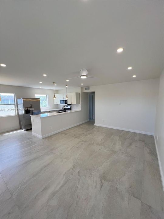 Open-concept interior featuring large-format tile flooring, recessed ceiling lighting, a kitchen island with stone-finish countertops, stainless steel appliances, and a central ceiling fan