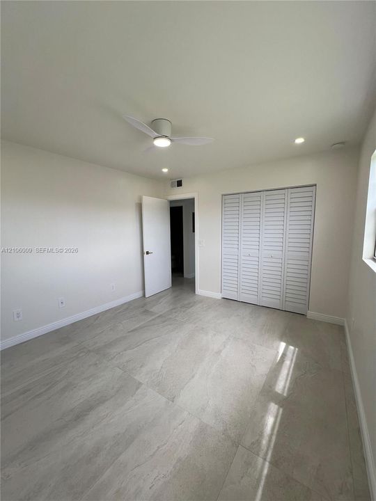 Large-format tile flooring, modern flush-mount ceiling fan, recessed lighting, and bifold louvered closet doors