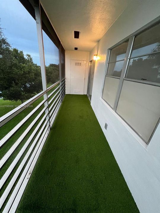 Screen-enclosed balcony featuring artificial turf flooring, metal railing, and recessed ceiling lighting