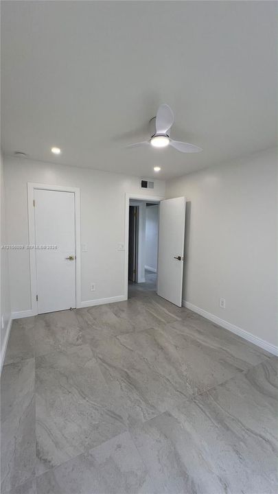 Large-format tile flooring, modern three-blade ceiling fan with integrated lighting, and recessed ceiling lights