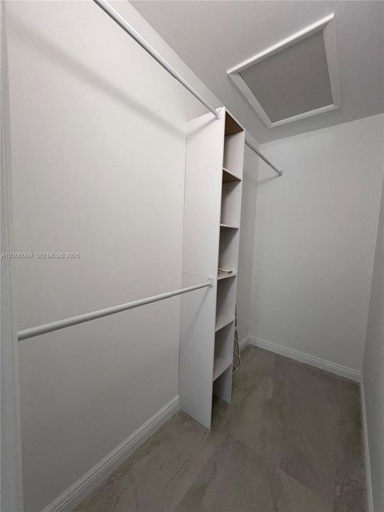 Walk-in closet featuring white built-in shelving, dual-tier hanging rods, and neutral-toned flooring