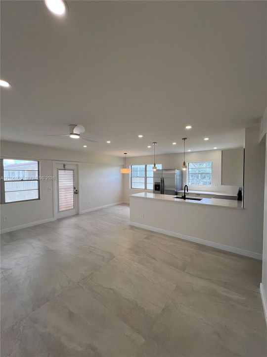 Open-concept interior featuring large-format tile flooring, recessed lighting, kitchen with quartz-surfaced island and bar seating, and stainless-steel appliances