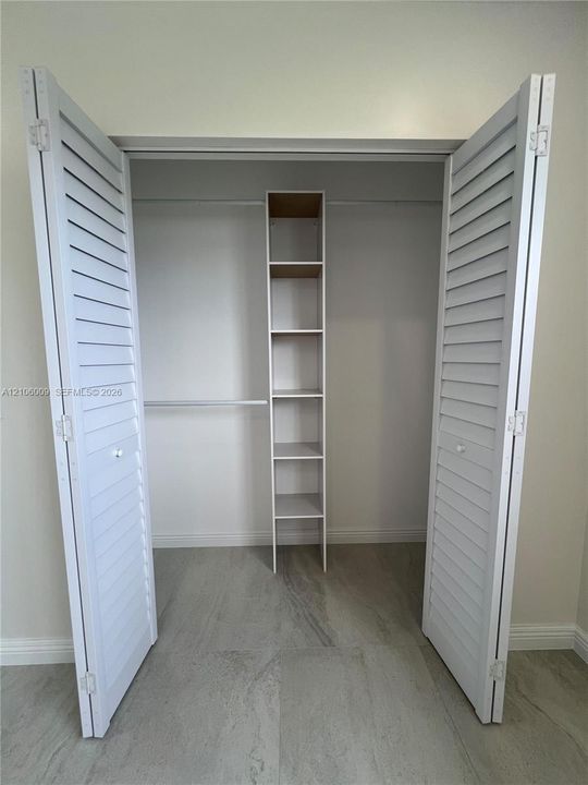 Closet featuring white louvered bifold doors, built-in shelving unit, and hanging rod