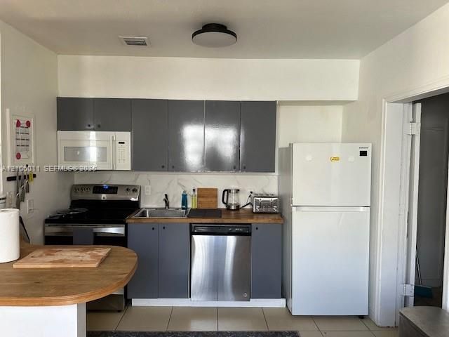 Kitchen featuring grey cabinetry, stainless steel dishwasher, built-in microwave, wood-finish countertop, and light-toned tile flooring