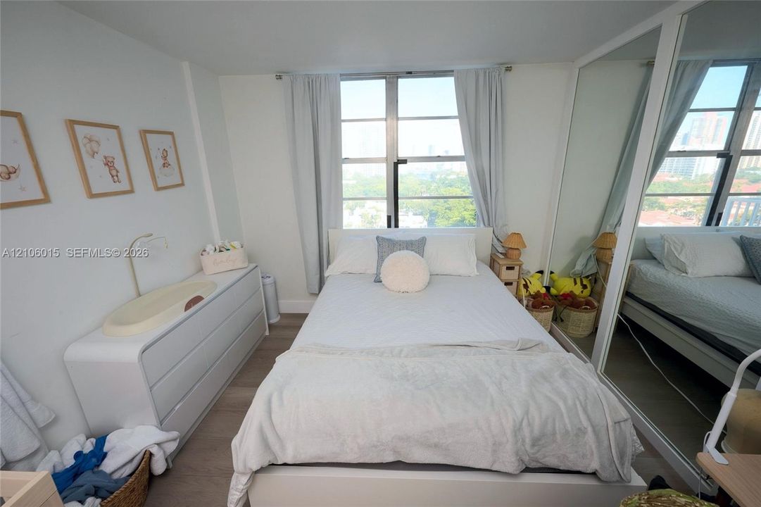 Bedroom featuring wood-finish flooring, large floor-to-ceiling windows, and wall-to-wall mirrored closet doors