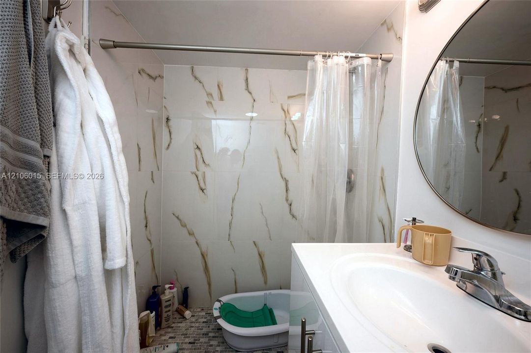 Full-height shower surround featuring large-format veined tile, vanity with a white integrated basin, polished chrome faucet, and round wall-mounted mirror
