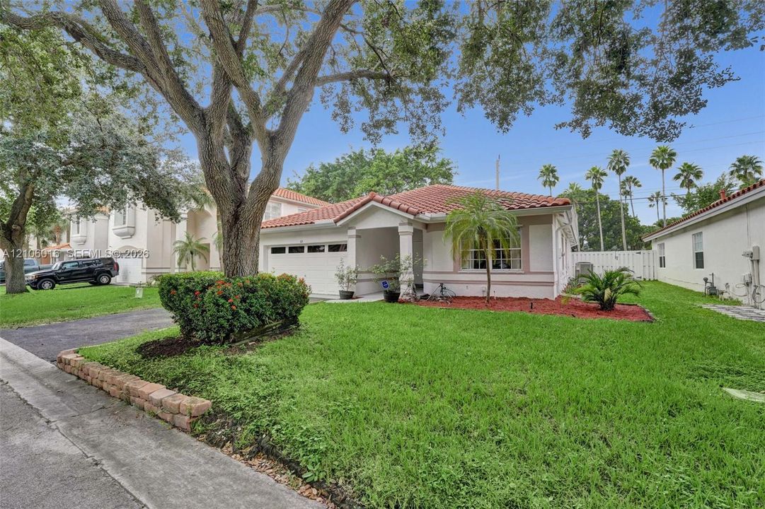 Single-story residence featuring a terracotta-tile roof, stucco exterior, integrated garage, concrete paver-style edging, and mature landscaping