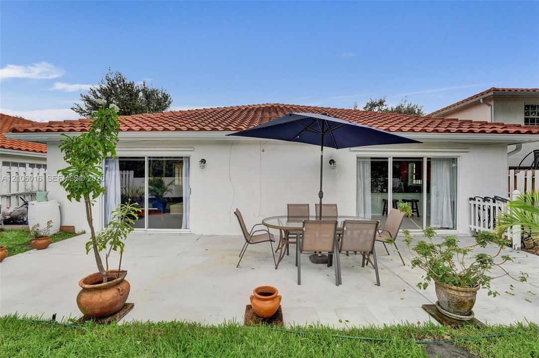 Concrete patio area featuring dual sliding glass doors, exterior wall-mounted lighting, and a terracotta tile roof