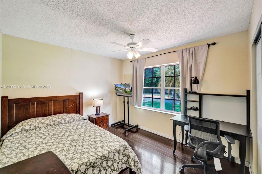 Room featuring wood-finish flooring, a multi-pane window with a curtain rod, and a ceiling-mounted light fixture with a fan