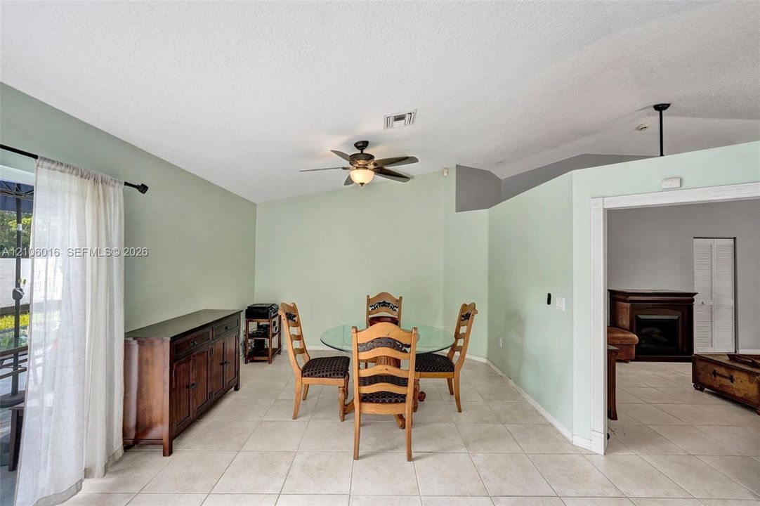Vaulted ceilings, neutral ceramic tile flooring, ceiling fan with integrated lighting, sliding glass door, and fireplace